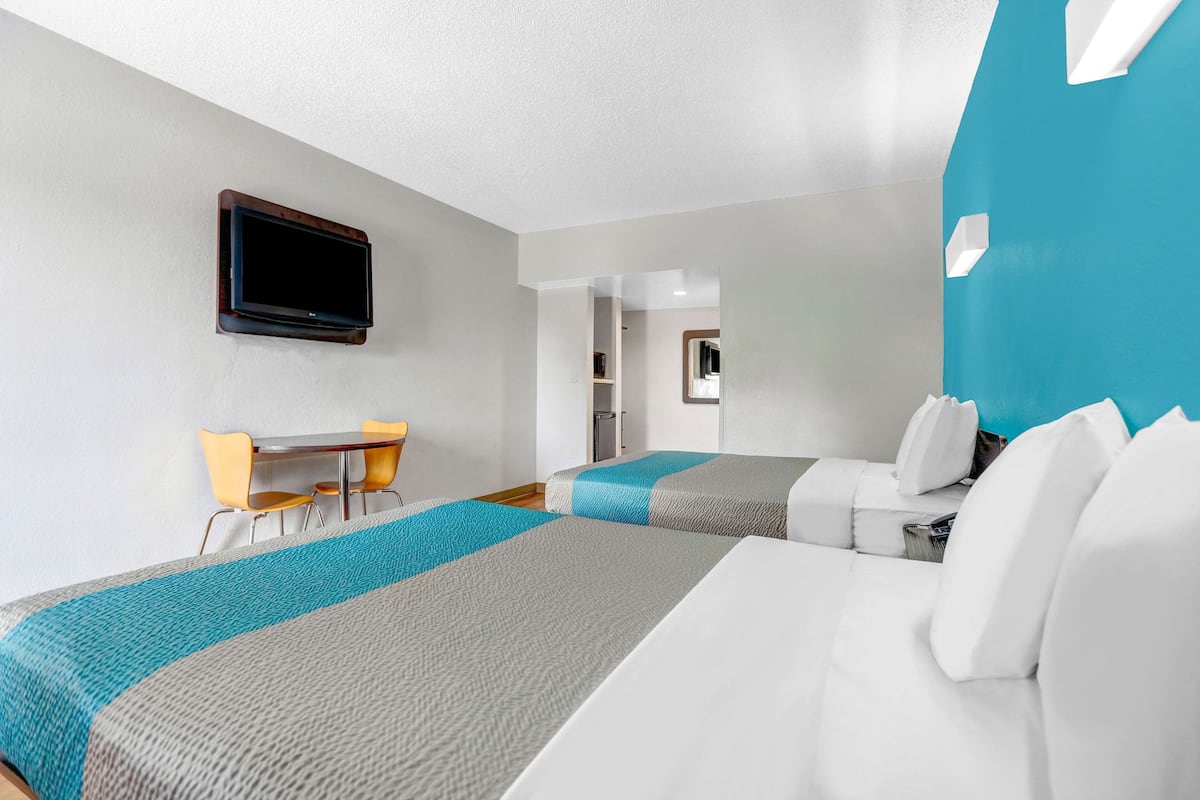 Habitación de hotel con dos camas, un escritorio y un televisor montado en la pared.