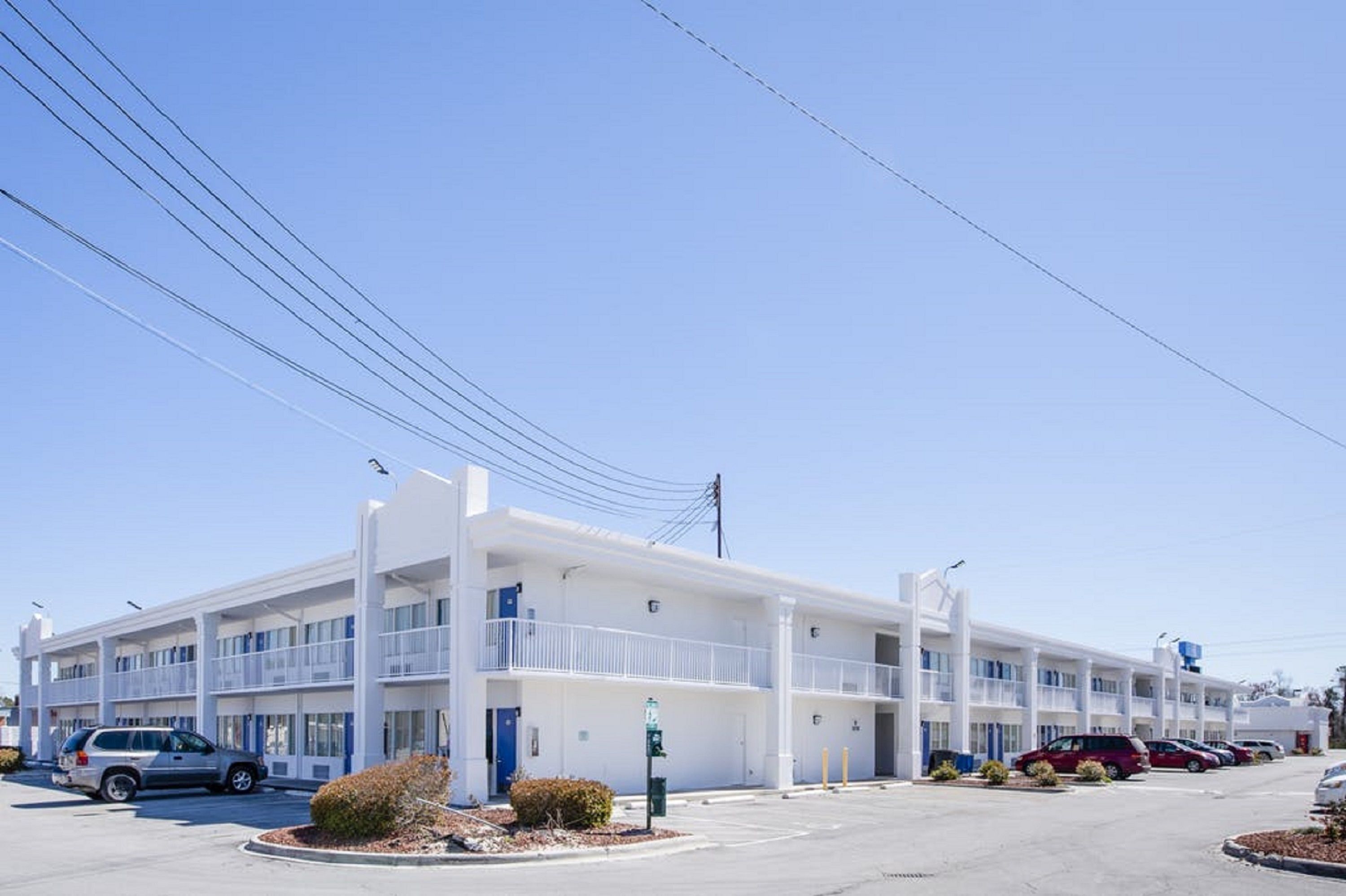 A multi-story motel with a central courtyard, parking lot, and a clear blue sky.