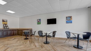 A modern interior with a herringbone-patterned floor, a white ceiling, and a flat-screen TV mounted on the wall. - Motel 6 Jacksonville, NC (Jacksonville)