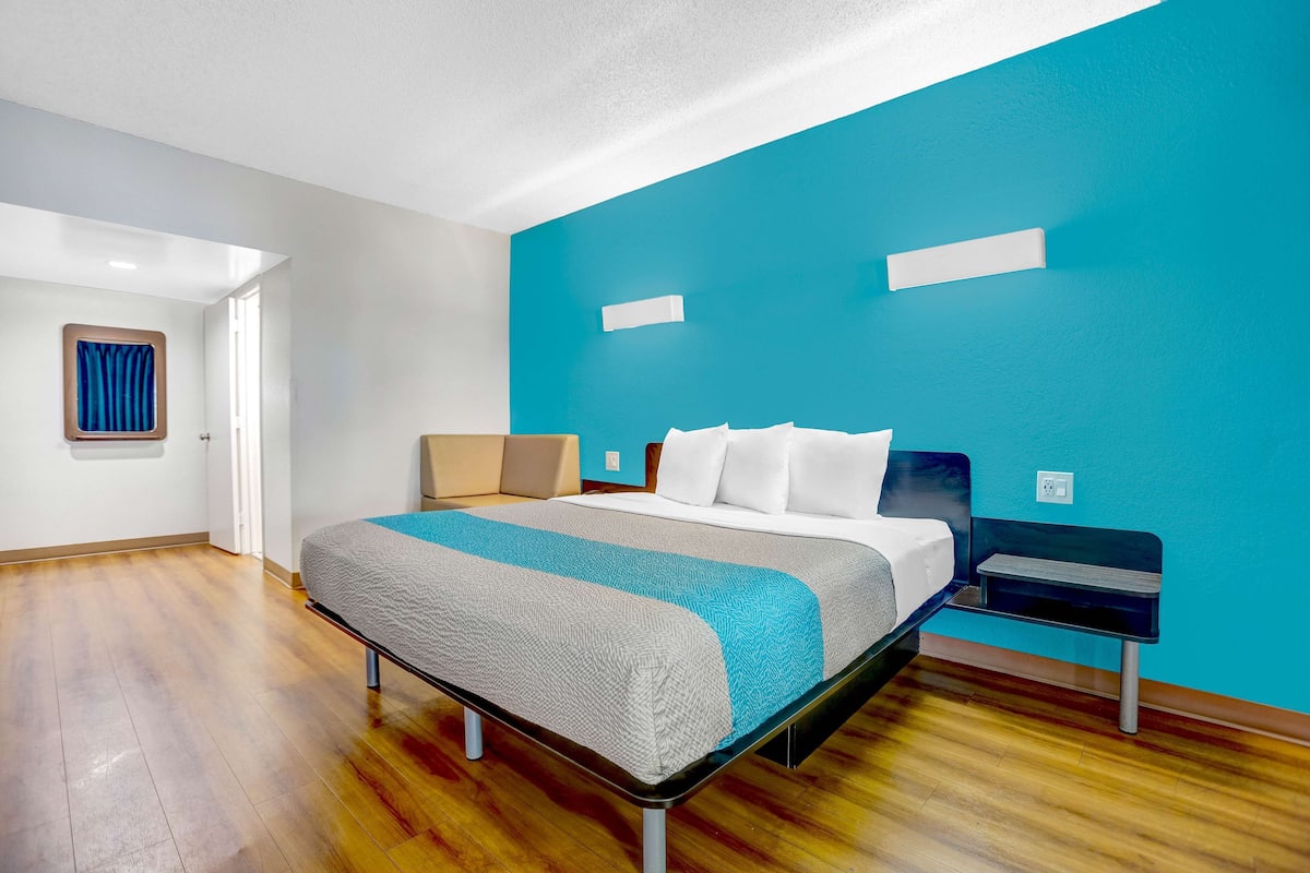 Una habitación de hotel moderna con una cama, una mesita de noche, una pared de acento azul y suelo de madera.