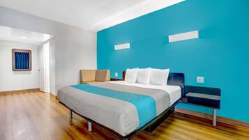A modern hotel room with a bed, a nightstand, a blue accent wall, and a wooden floor.