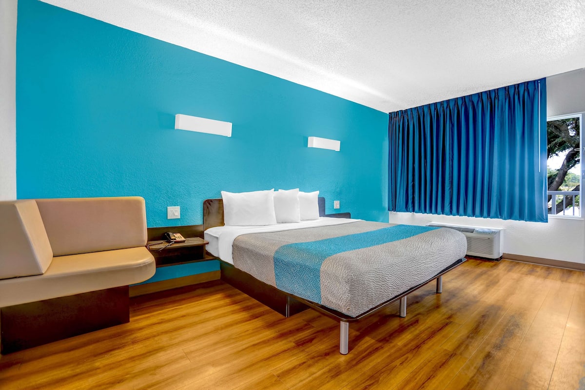 Una habitación de hotel moderna con cama, sofá, ventana con cortinas y suelo de madera.
