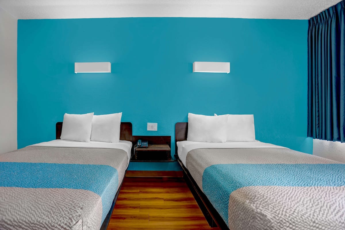 Habitación de hotel con dos camas, suelo de madera y una pared color aguamarina.