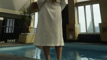 A woman in a white robe standing by a pool with a glass ceiling above.