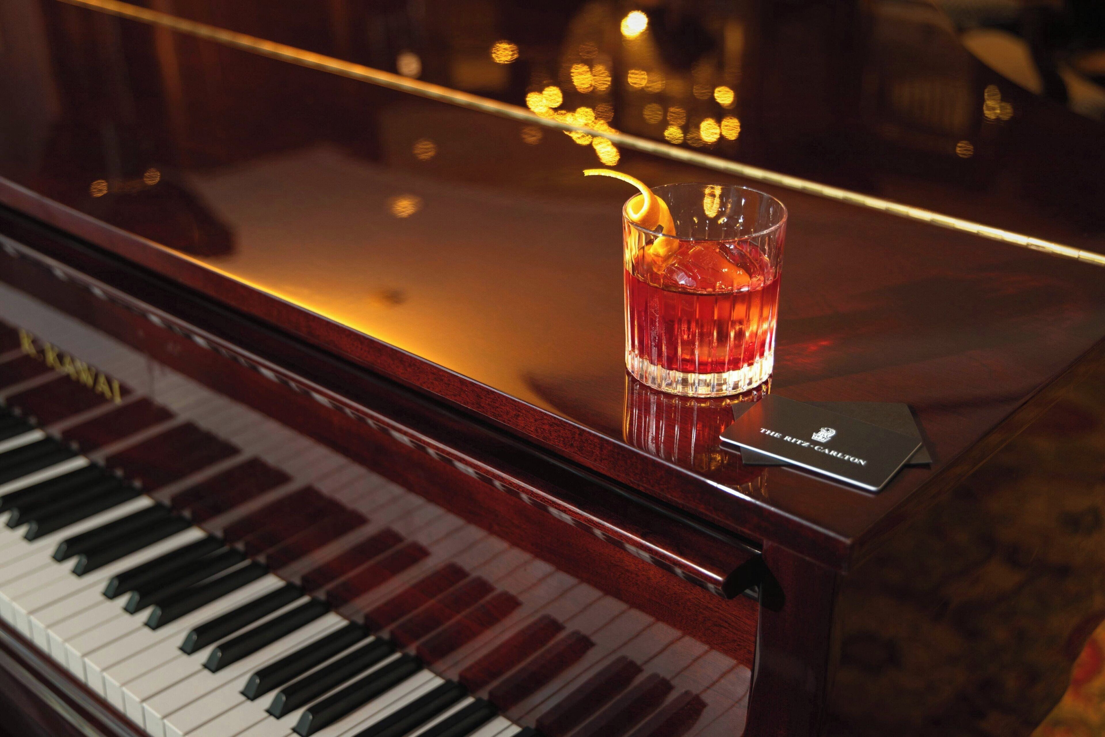 Un piano de cola con un vaso de bebida roja y un menú en el atril.