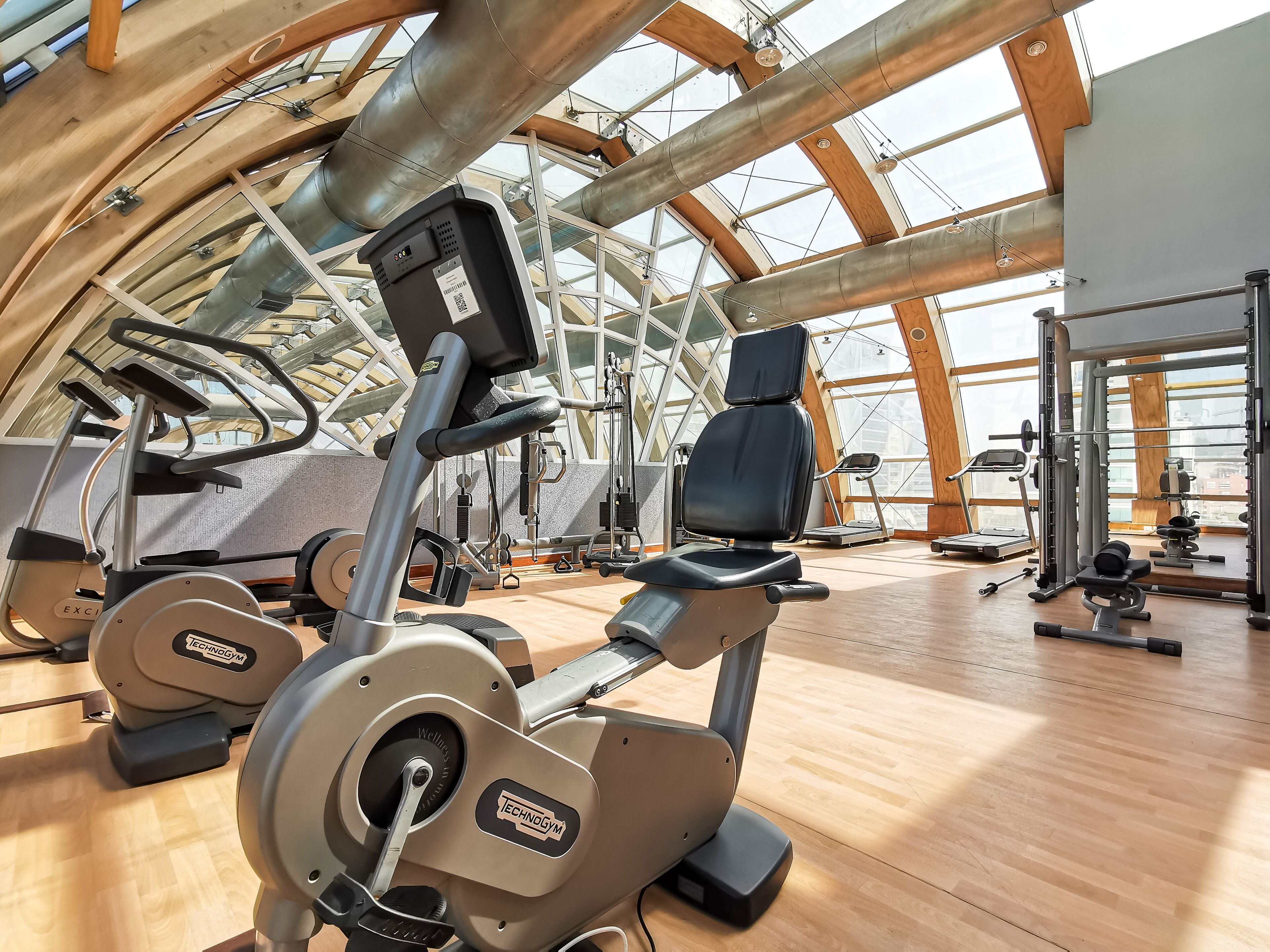 Uma academia com diversos equipamentos de exercício, uma janela grande e piso de madeira.