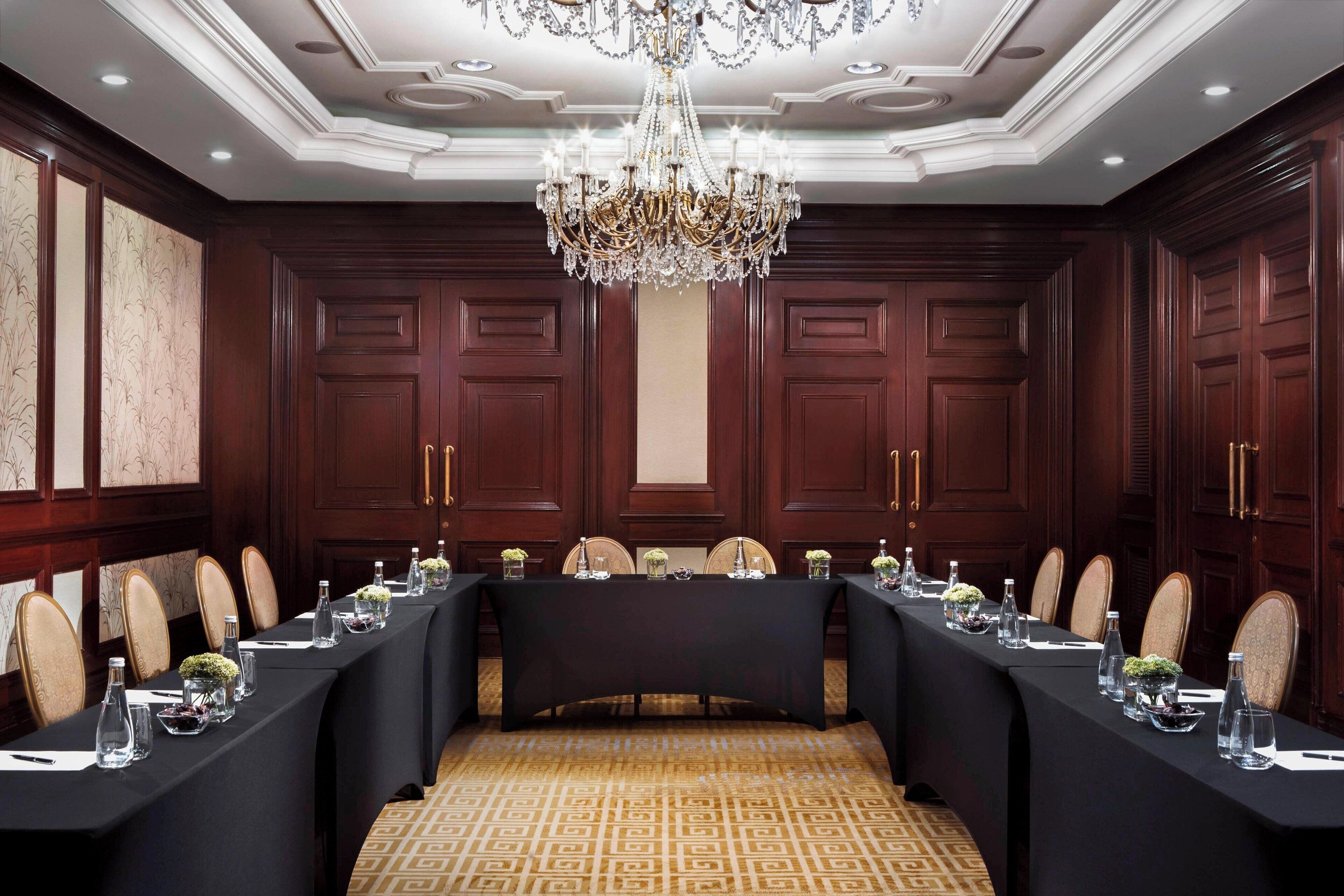 A formal meeting room with a long table, chairs, and a chandelier.