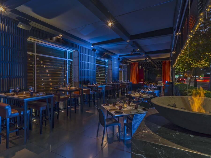 Un comedor interior con mesas y sillas, una chimenea y vistas de la ciudad de noche.