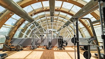 Een sportschool met een hoge plafond en dakramen, met diverse fitnessapparaten en een houten vloer.