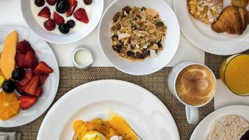 Una mesa de desayuno con diversos platos, entre ellos huevos benedictinos, croissants y fruta.