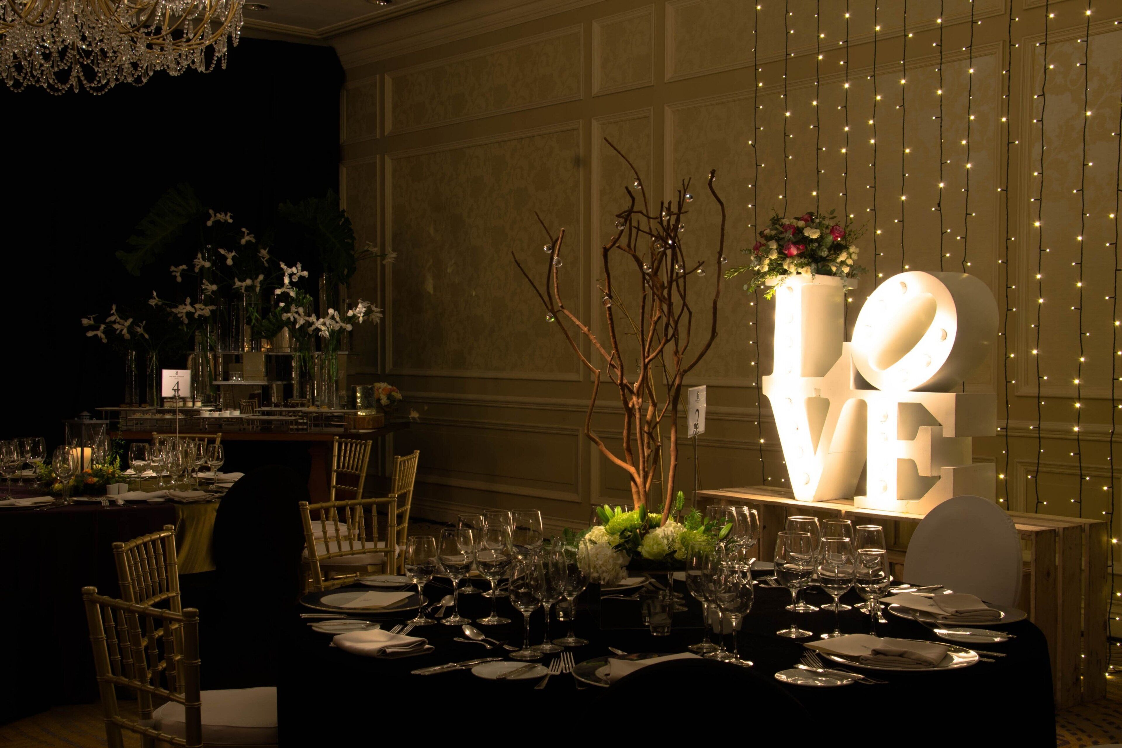 A formal dining setup with tables set for multiple guests, a decorative centerpiece, and a large illuminated sign that reads "LOVE".