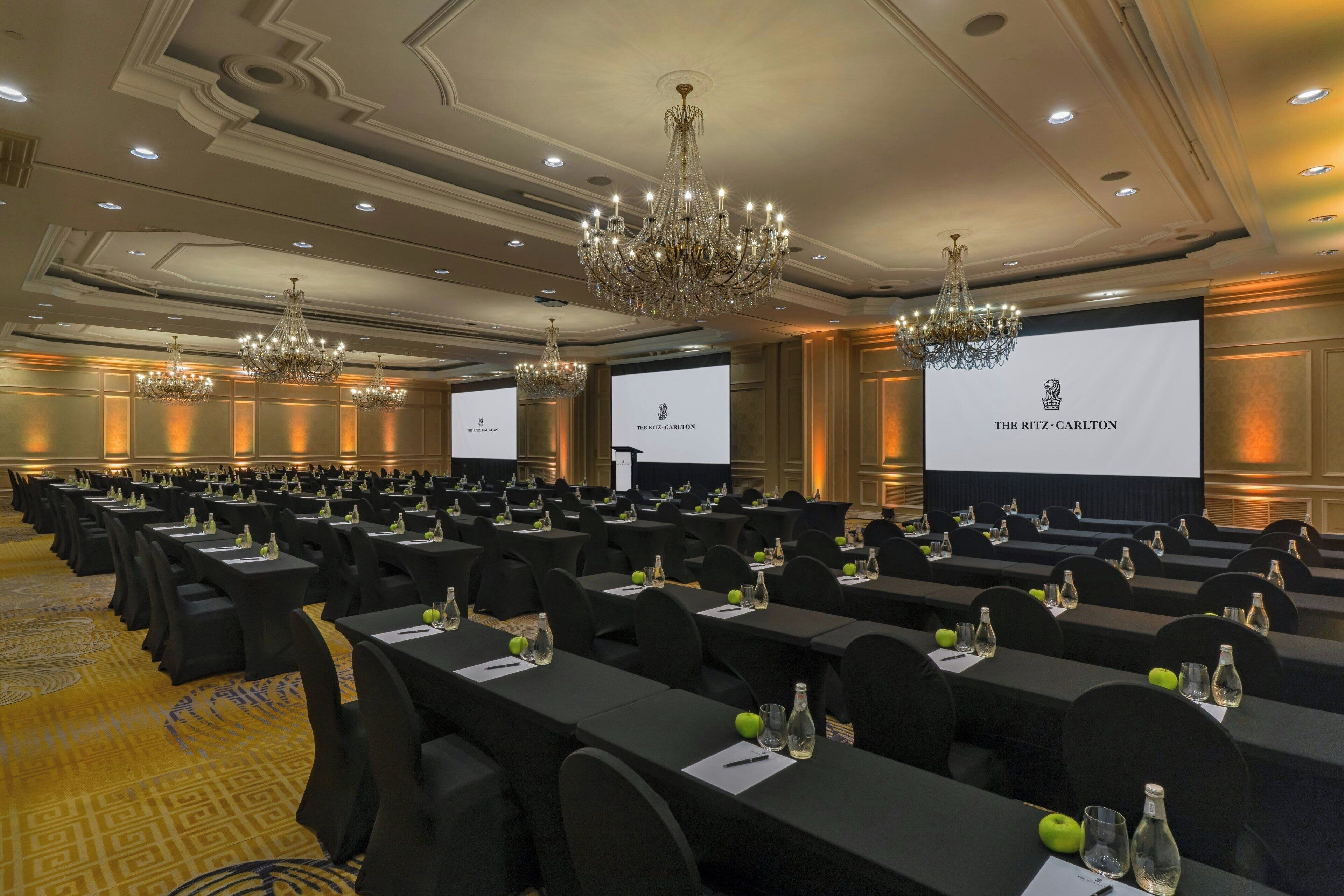 Un salón de conferencias con filas de mesas, sillas negras y candelabros.