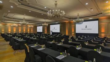 Un salón de conferencias con filas de mesas, sillas negras y candelabros.