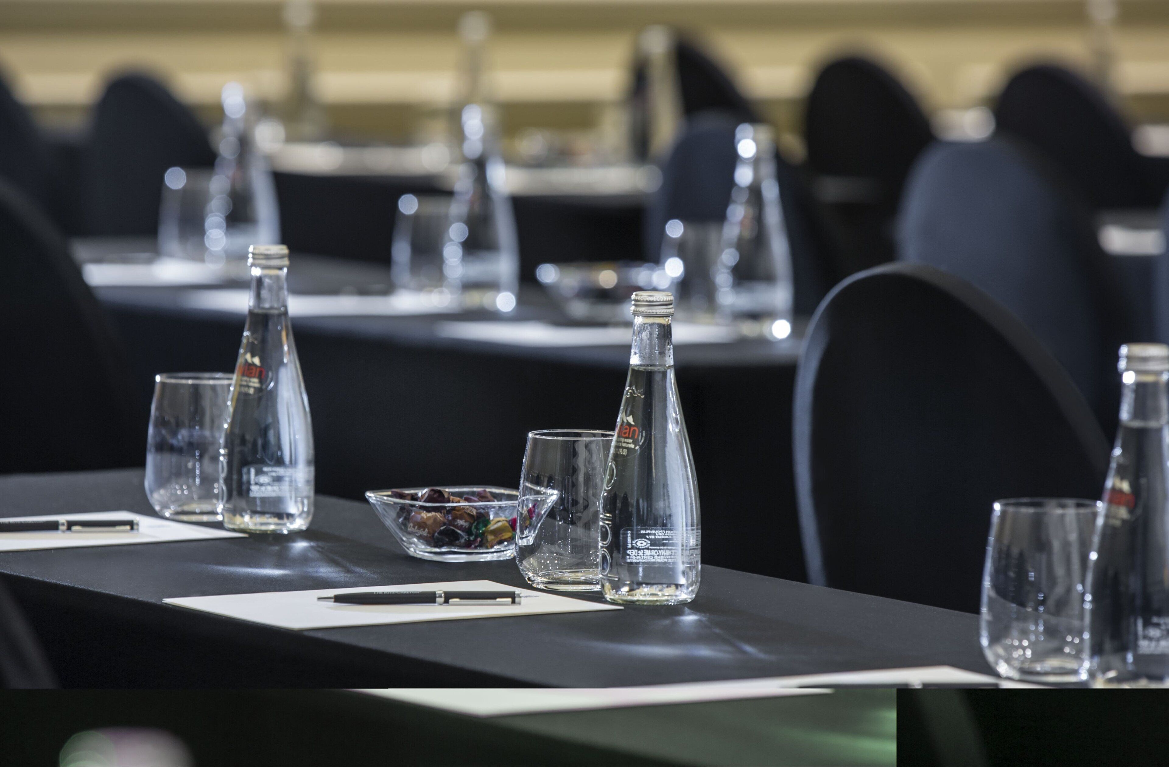 Una mesa de conferencias con una botella, vasos y un tazón de bocadillos.