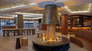 Un espace de détente moderne doté d’un foyer central, de différents coins salon et d’un bar.