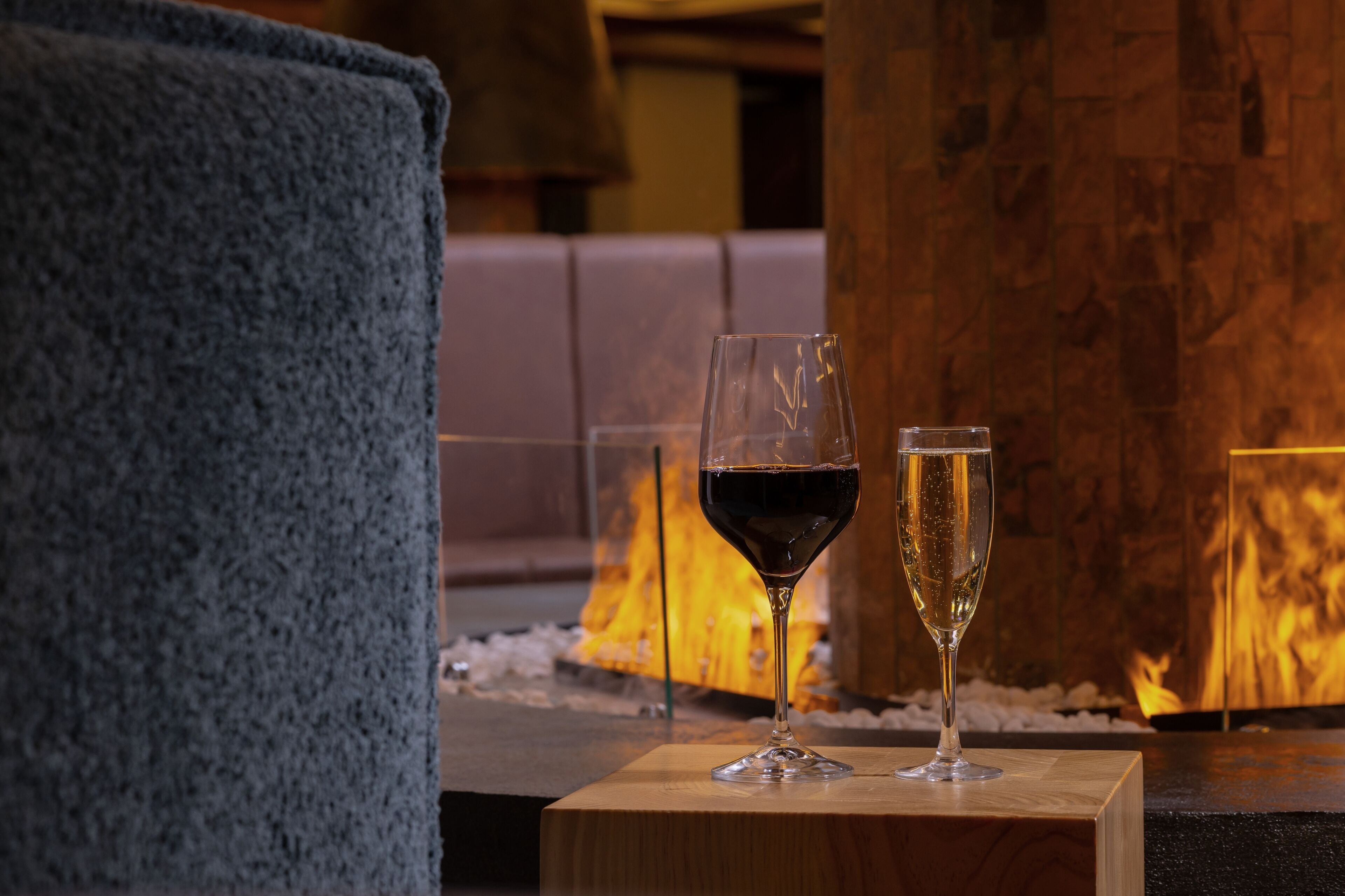 Una mesa de madera con dos copas de vino, una toalla azul y una chimenea al fondo.