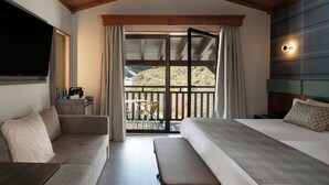 Une chambre dotée d’un grand lit, d’un canapé, d’une banquette, d’une télévision et d’un balcon offrant une vue sur l’extérieur.