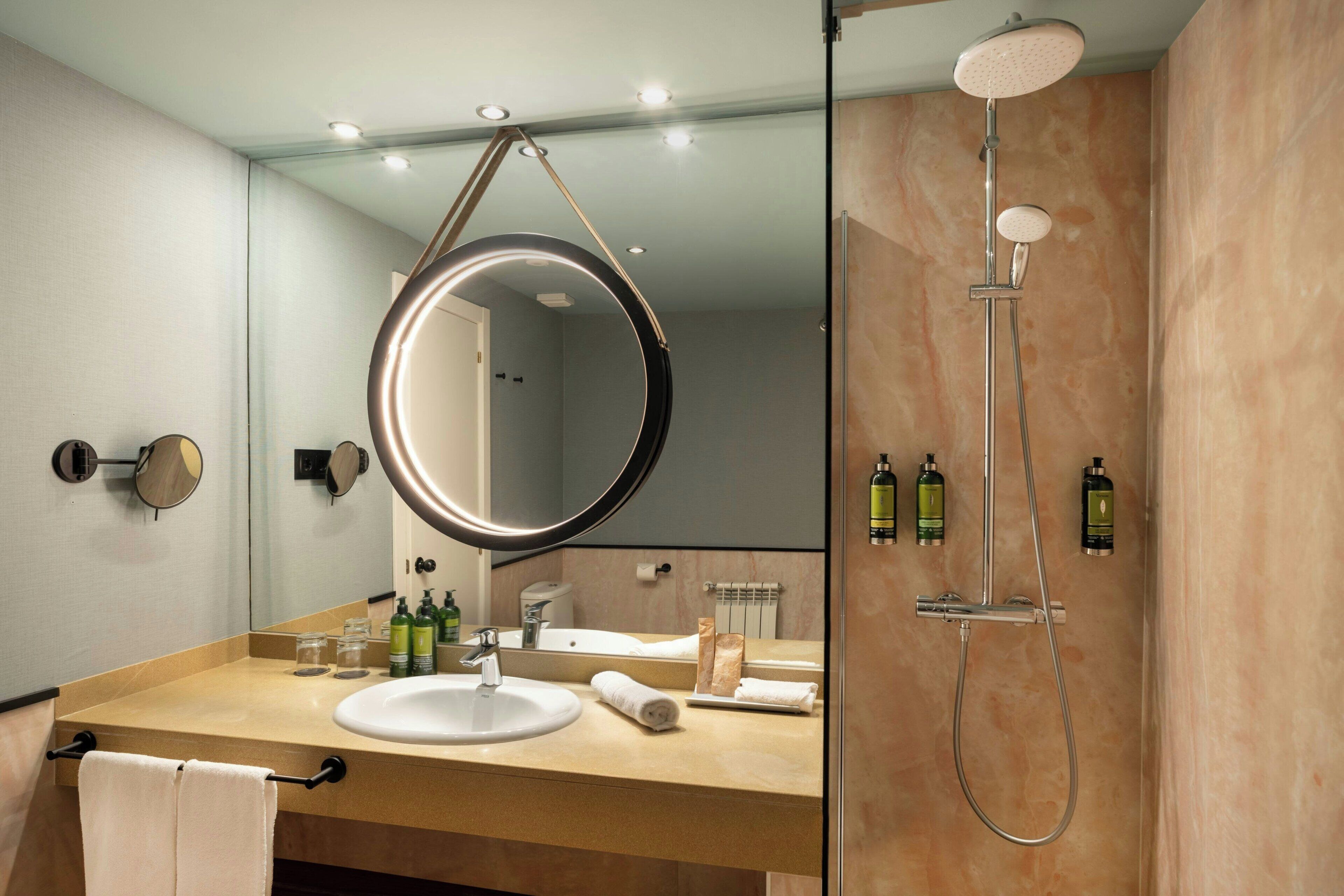 Un bagno moderno con uno specchio rotondo, un lavandino e una doccia.