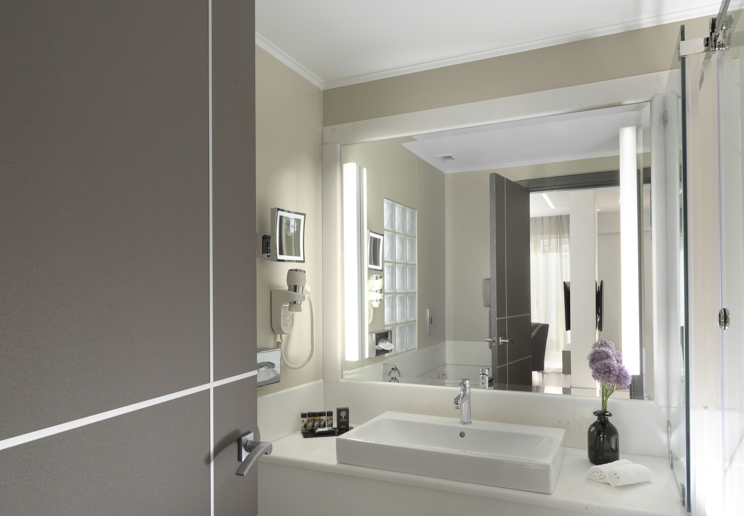 A modern bathroom with a large mirror, a white sink, and a glass shower enclosure.