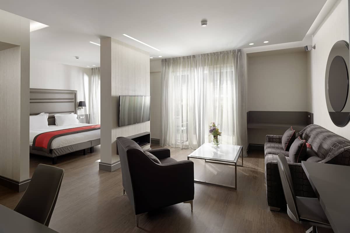 A modern hotel room with a bed, a sofa, a coffee table, and a TV.