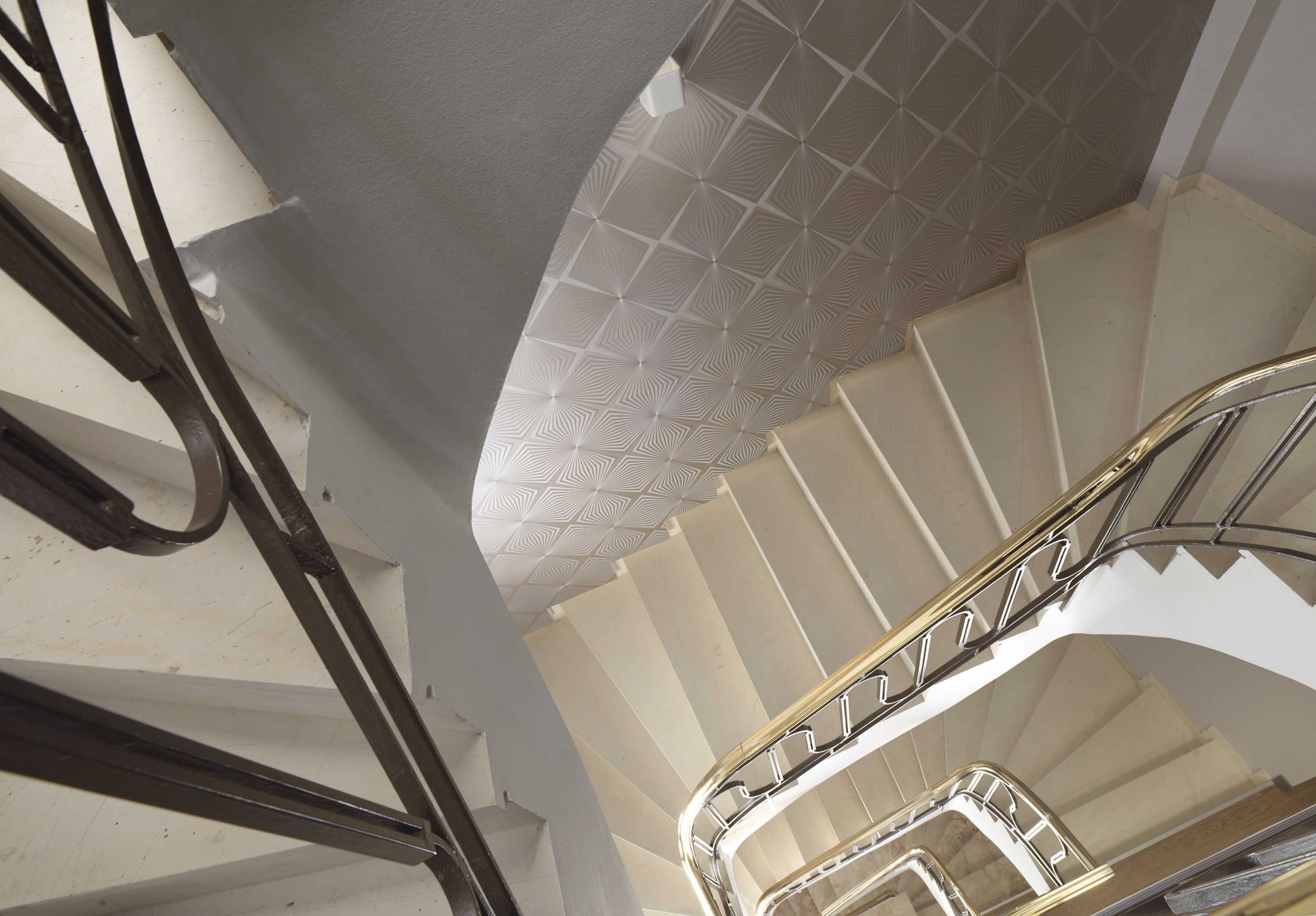 A spiral staircase with a geometric patterned ceiling and metal handrails.
