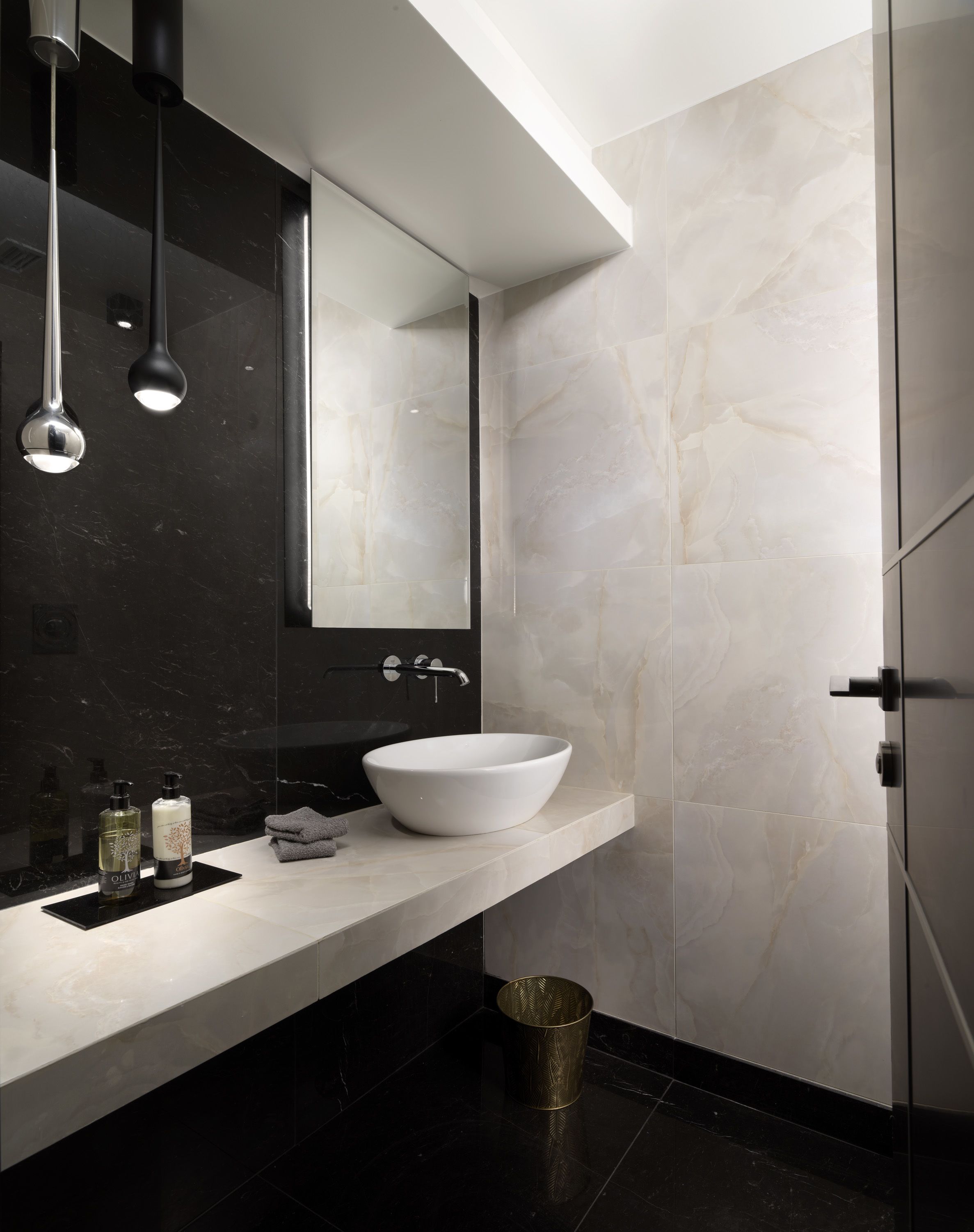 Un bagno moderno con un lavabo a incasso bianco, pareti in marmo nero e un grande specchio.