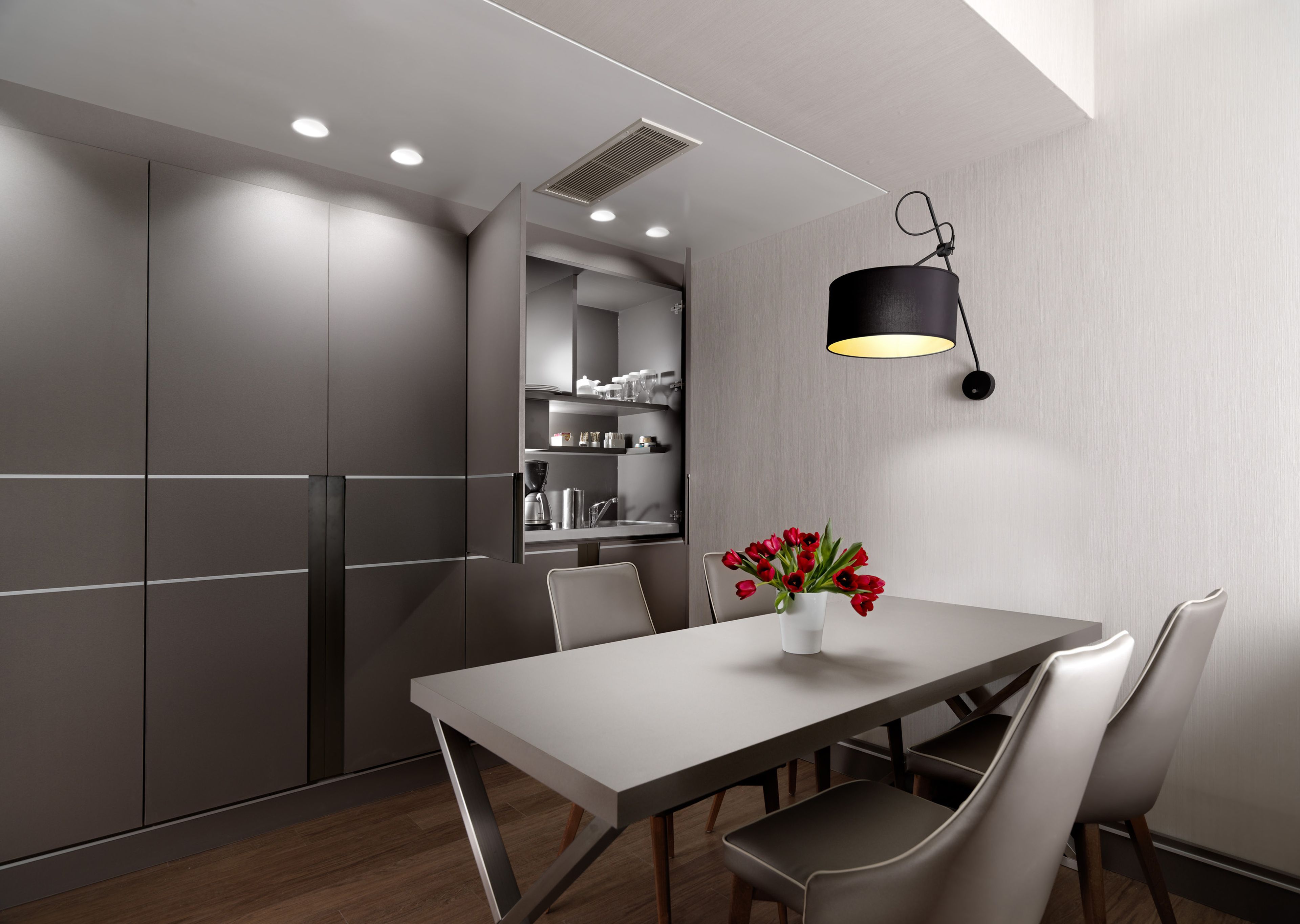 Una cocina moderna con zona de comedor, con una mesa larga, sillas, un florero con flores rojas y una lámpara colgante.