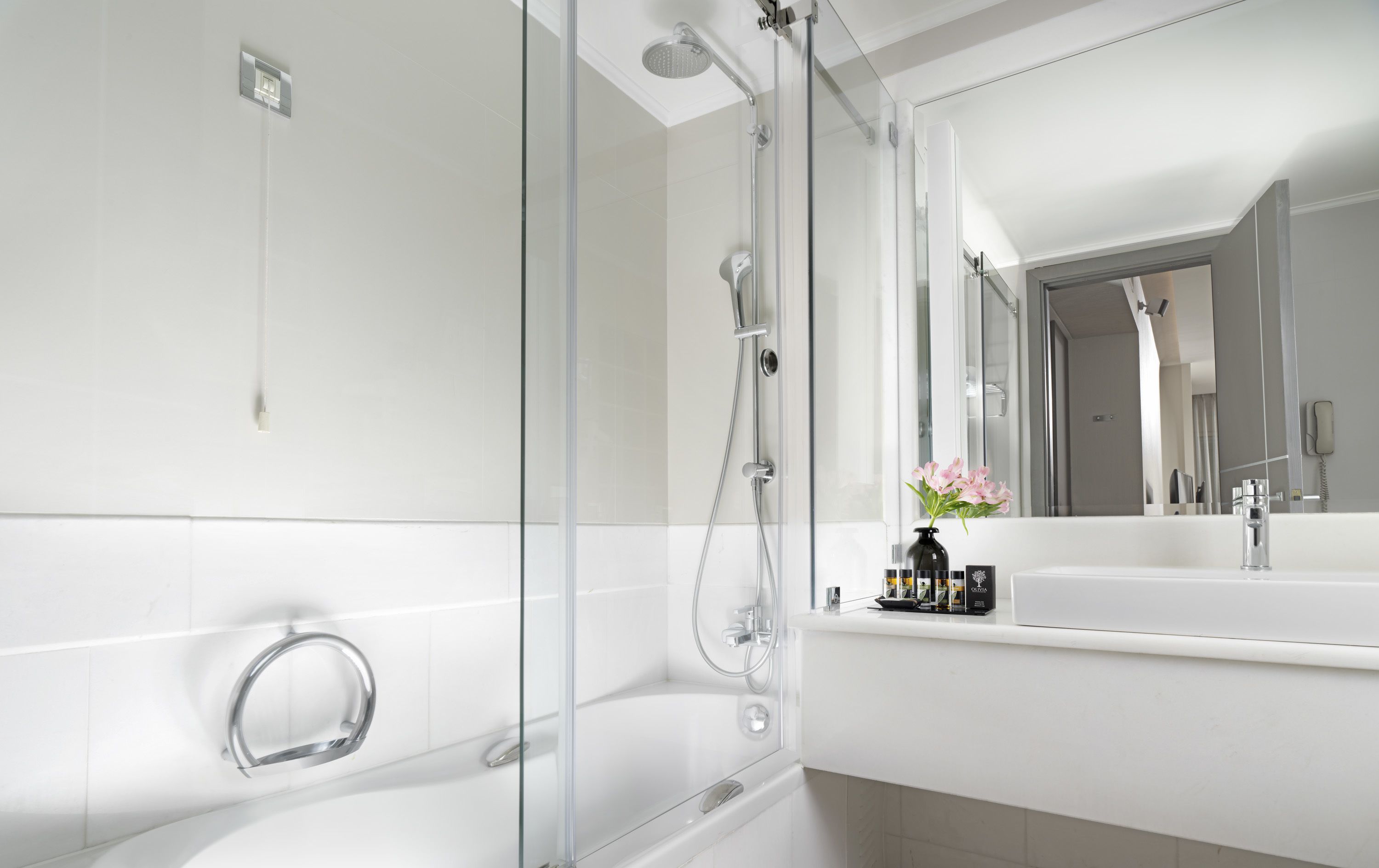 A modern bathroom with a glass-enclosed shower, a large mirror, and a white countertop with toiletries.