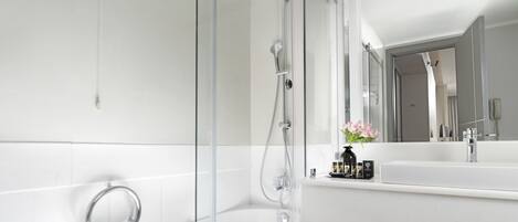 A modern bathroom with a glass-enclosed shower, a large mirror, and a white countertop with toiletries.