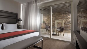 Une chambre d’hôtel moderne avec un grand lit, un banc, un bureau et un mur en pierre.