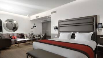 A modern hotel room with a large bed, a sofa, a desk, and a mirror.