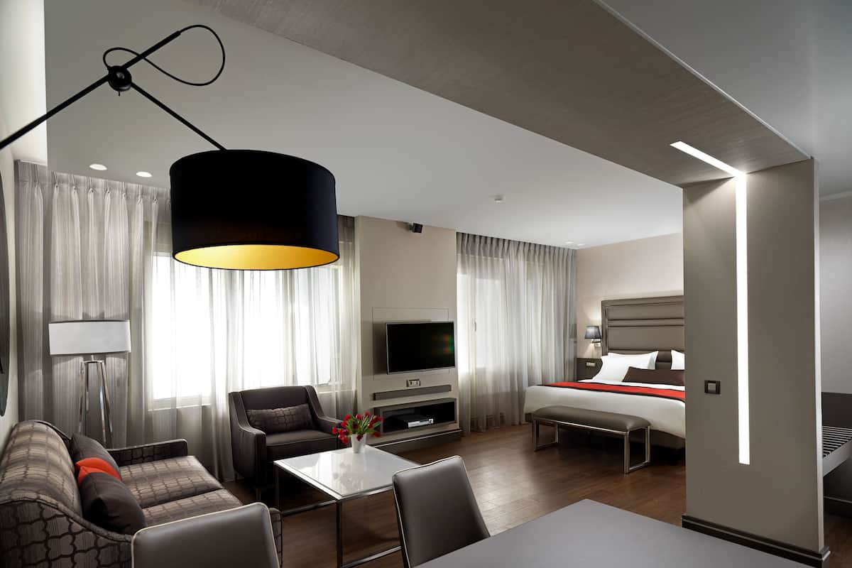 A modern hotel room with a sofa, a dining table, a TV, and a bed.