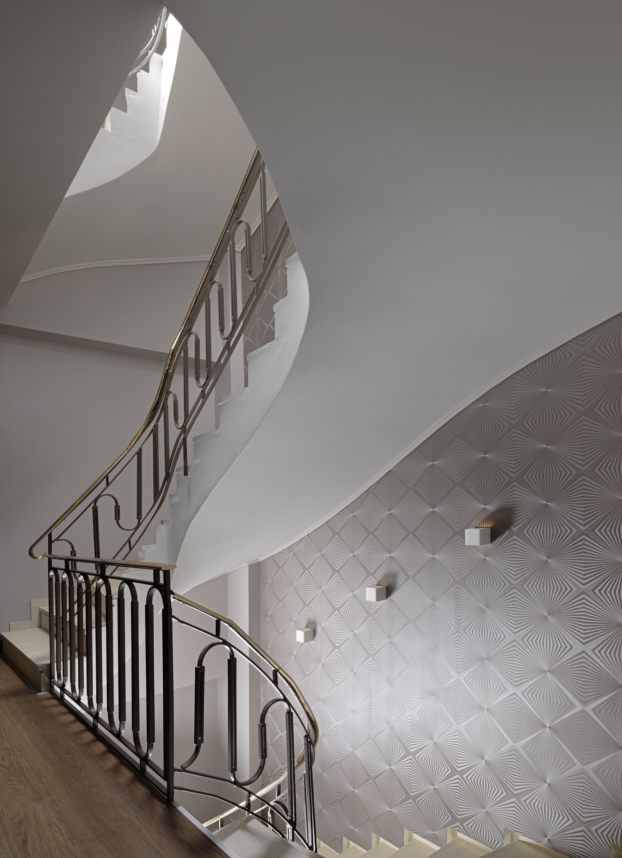 A modern staircase with a curved design, metal railings, and a patterned wall.
