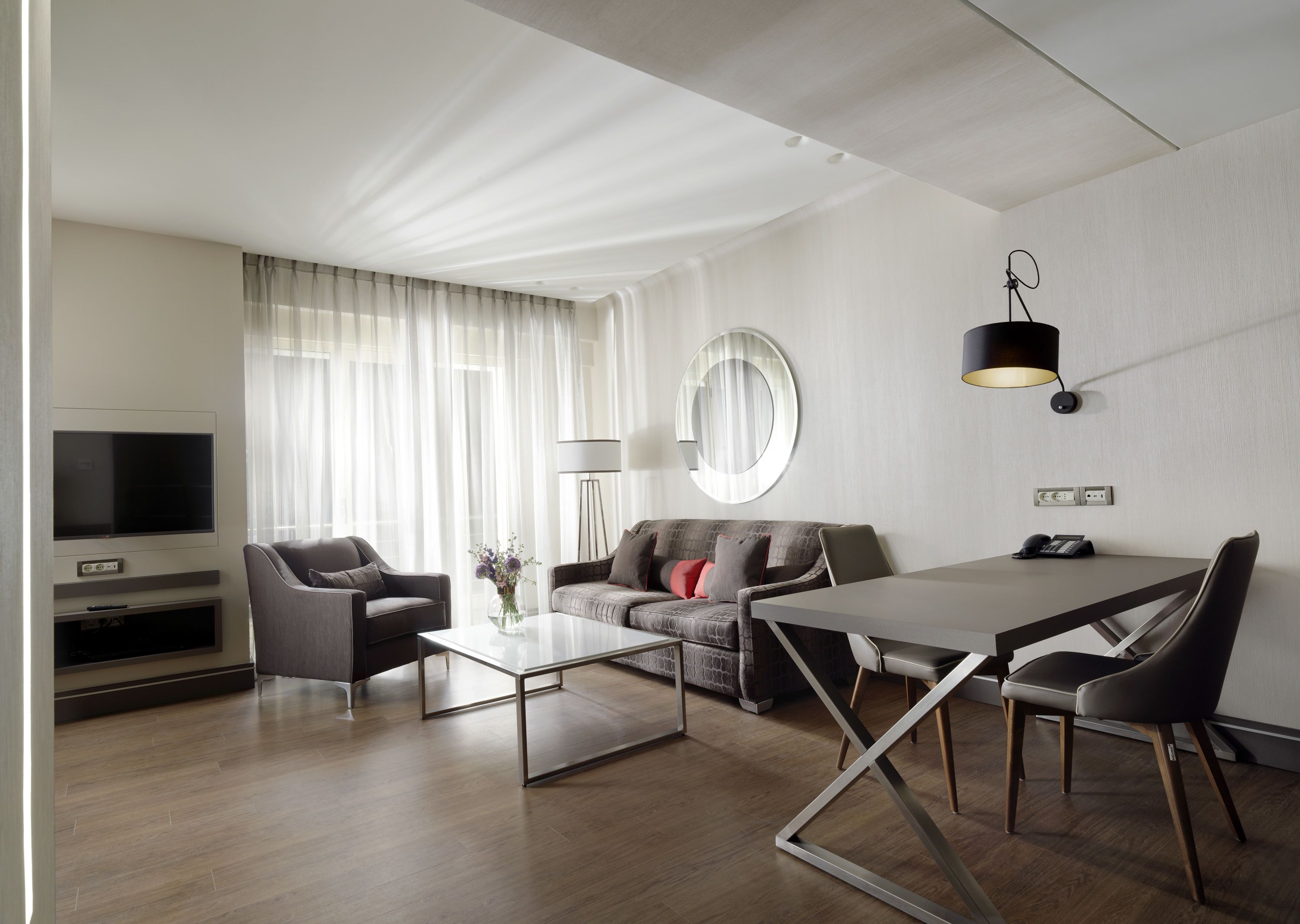 A modern living room with a flat-screen TV, a sofa, a coffee table, and a dining area with a table and chairs.