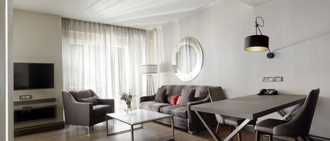 Una sala moderna con una televisión de pantalla plana, un sofá, una mesa de centro y un comedor con una mesa y sillas.