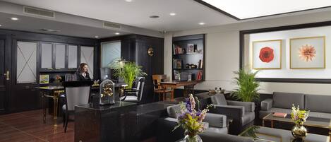 A modern hotel lobby with a reception desk, seating area, and a bookshelf.