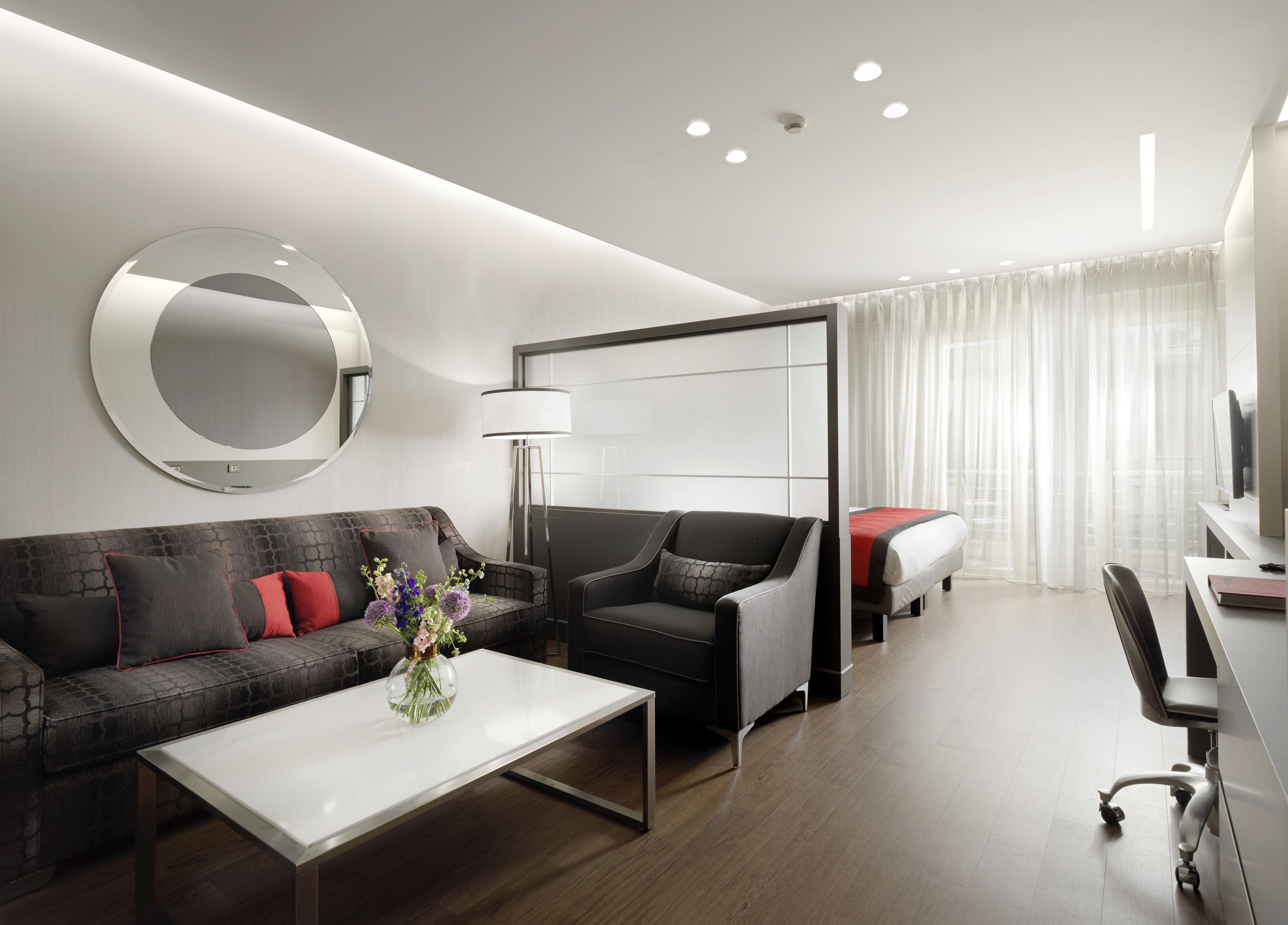 Een moderne hotelkamer met een bank, fauteuil en een bijzettafeltje met een bloevas.