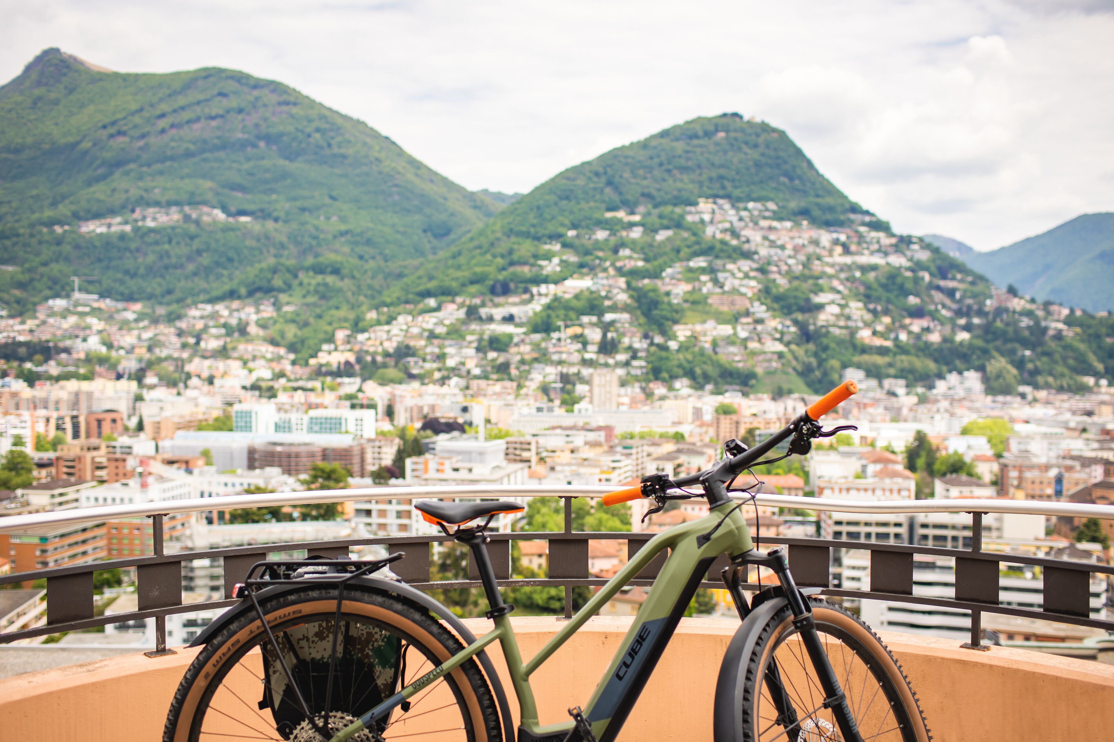 Uma bicicleta estacionada numa varanda com vista para a paisagem urbana e montanhas ao fundo.