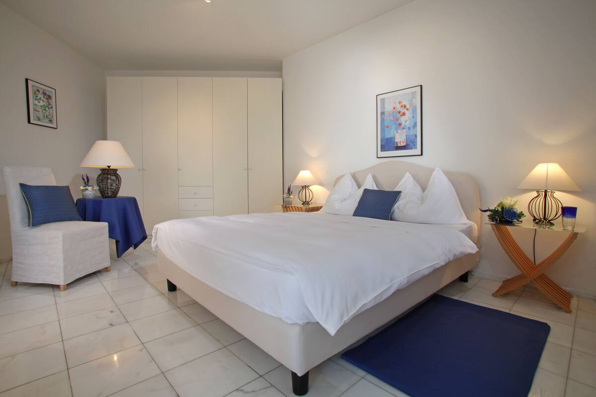 A bedroom with a large bed, a chair, a nightstand, and a wardrobe.