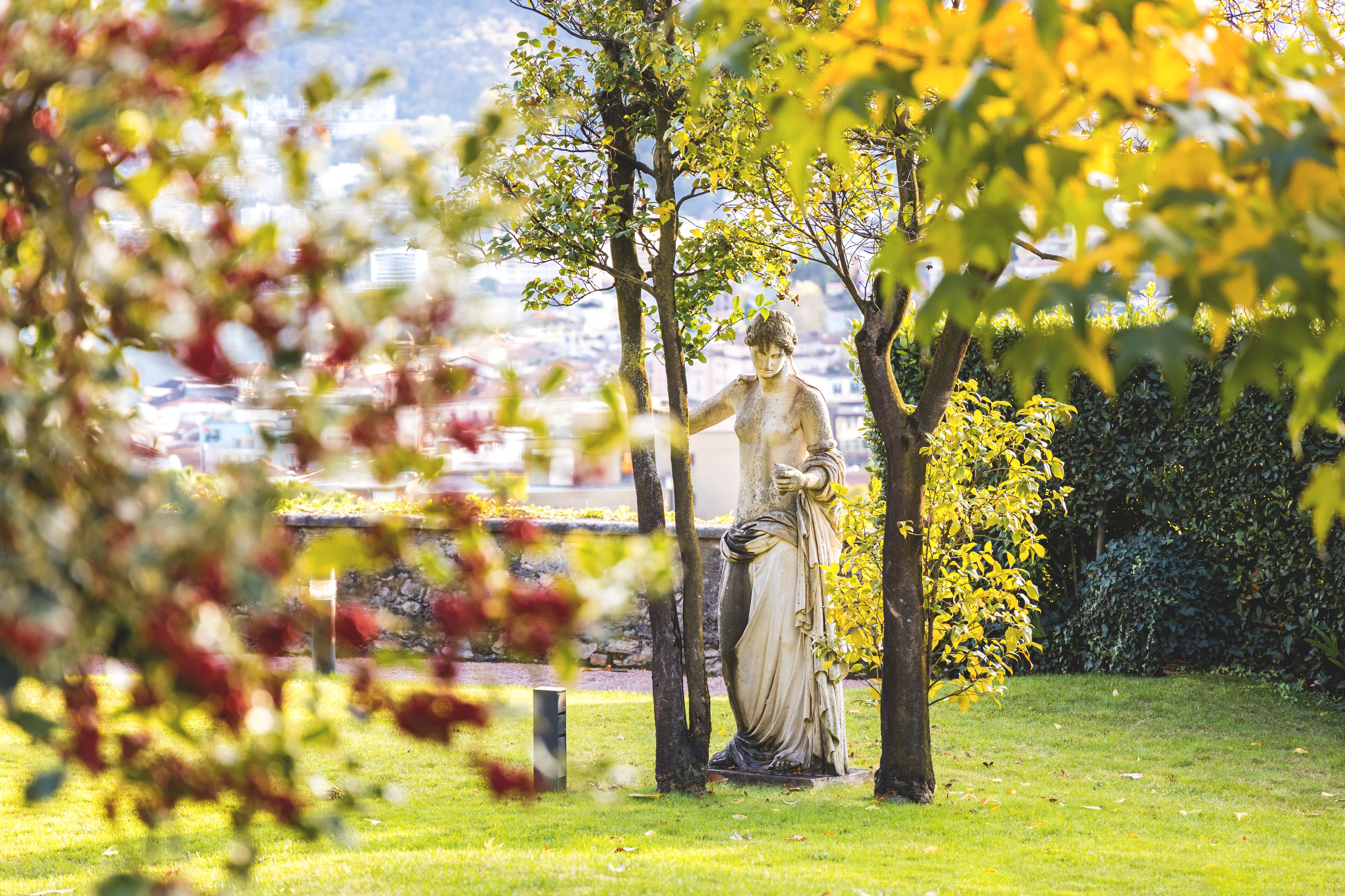 A statue in a park with a view of a cityscape in the background.