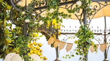 A wrought iron structure adorned with ivy and white roses, with bunting flags and decorative plates.