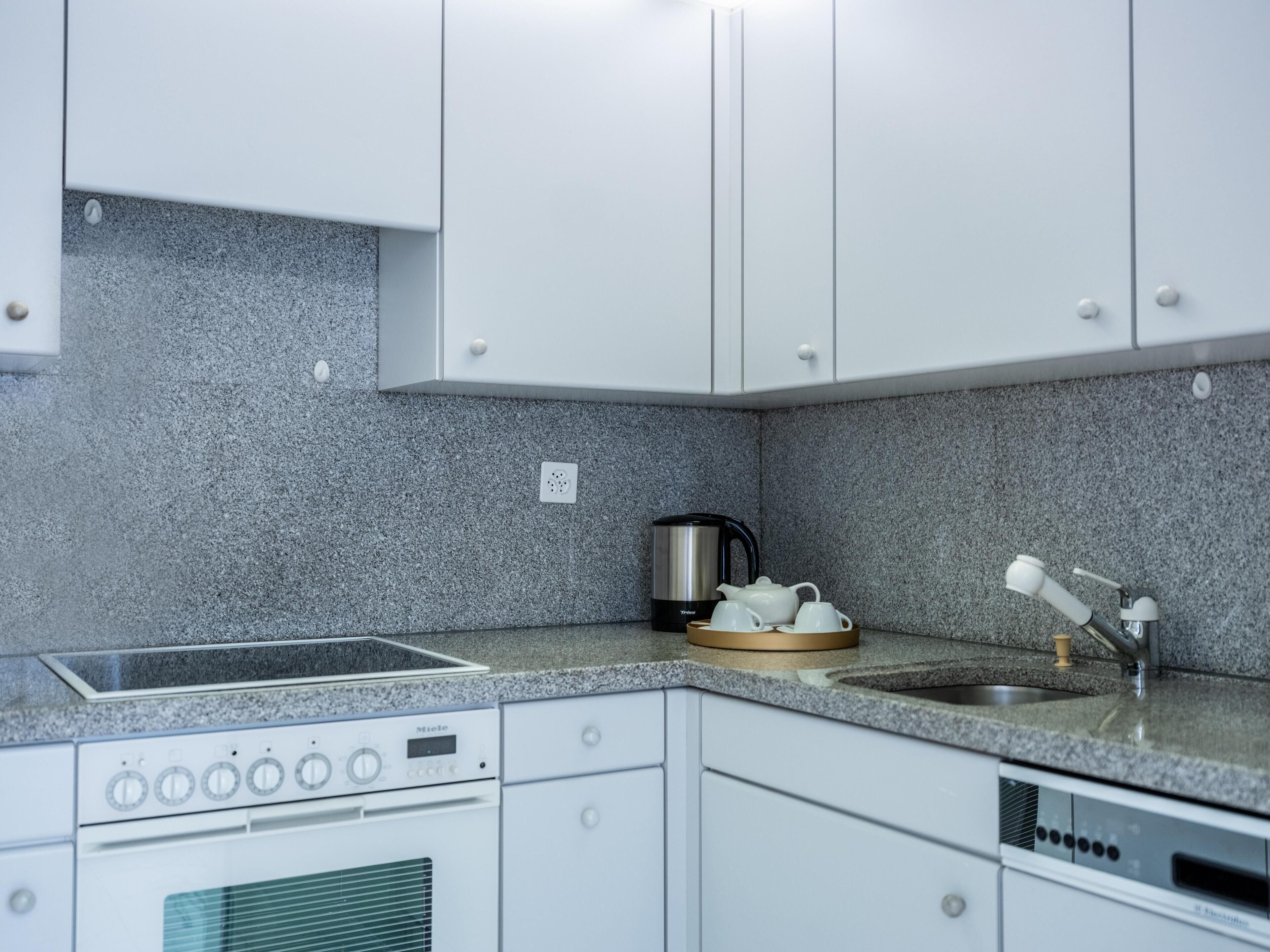Una cocina moderna con armarios blancos, encimera de granito, cafetera, hervidor y lavabo.