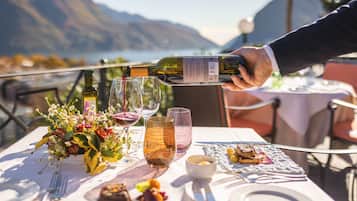 Una mesa dispuesta para una comida, con vino siendo servido, rodeada de copas y un centro de mesa floral, con una vista panorámica de las montañas al fondo.
