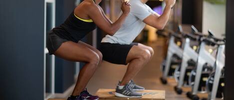 Two people performing squats in a gym with exercise equipment in the background.