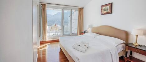 Habitación de hotel con una cama grande, una mesita de noche con lámpara, vista a montañas a través de una puerta corrediza de vidrio y un cuadro en la pared.