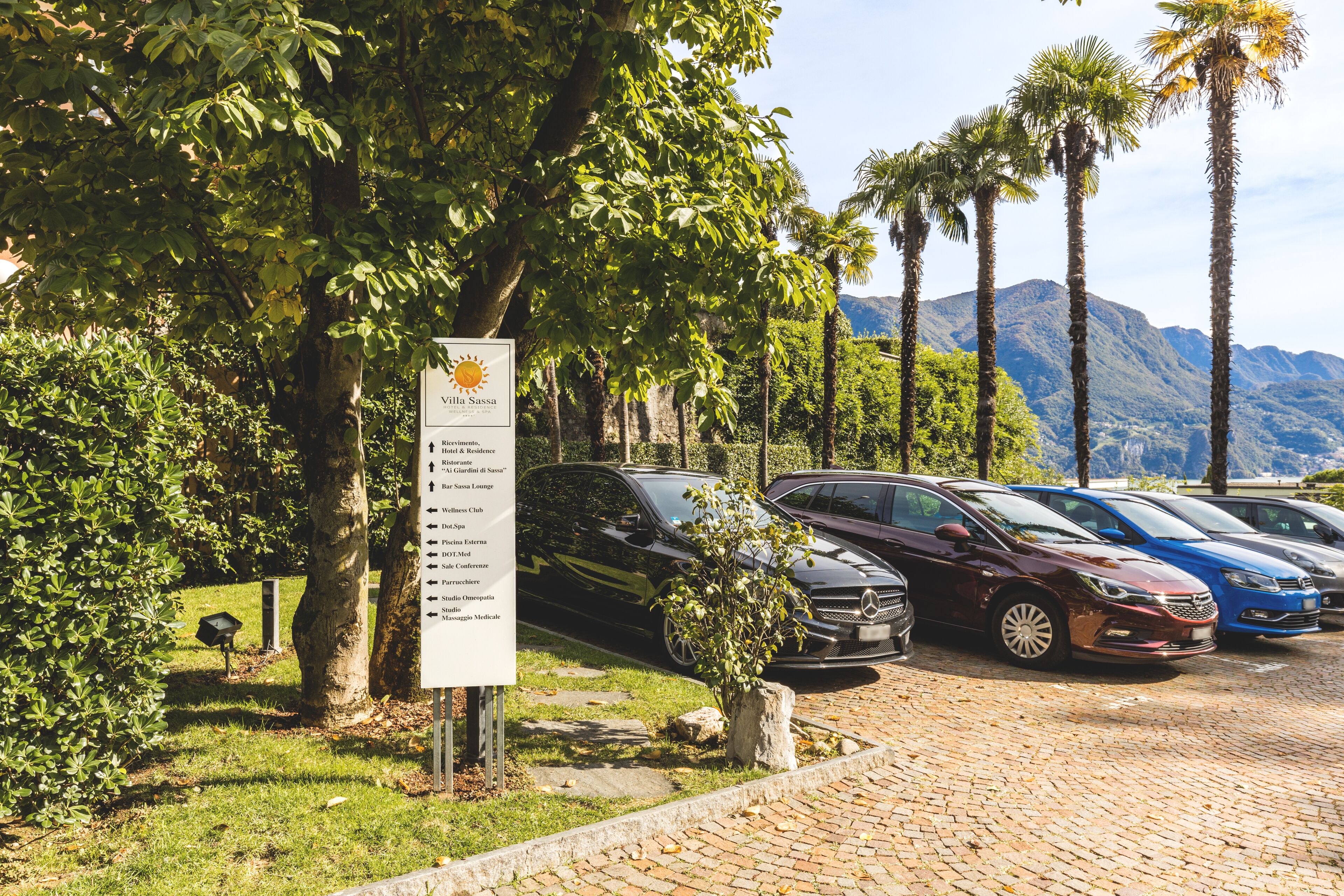 A parking area with several cars, a sign listing amenities, and a mountainous backdrop.