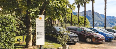 A parking area with several cars, a sign listing amenities, and a mountainous backdrop.