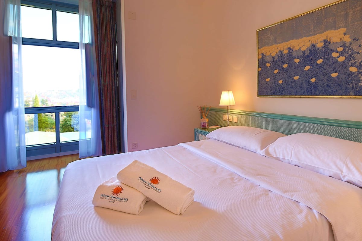 A hotel room with a large bed, a nightstand, a lamp, and a painting on the wall.