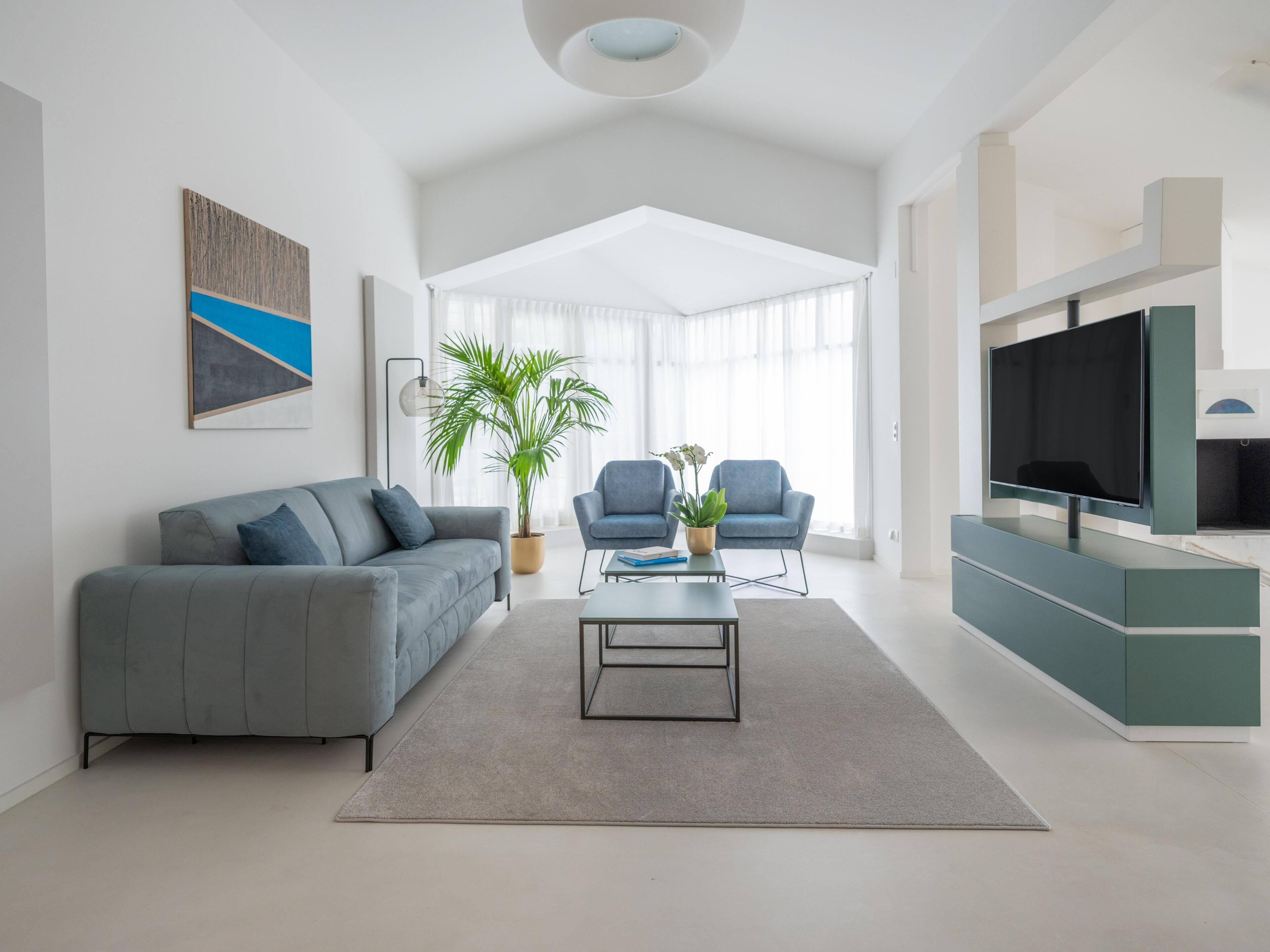 Una sala de estar moderna con un sofá gris, dos sillones, una mesa de centro, un televisor y un ventanal grande.