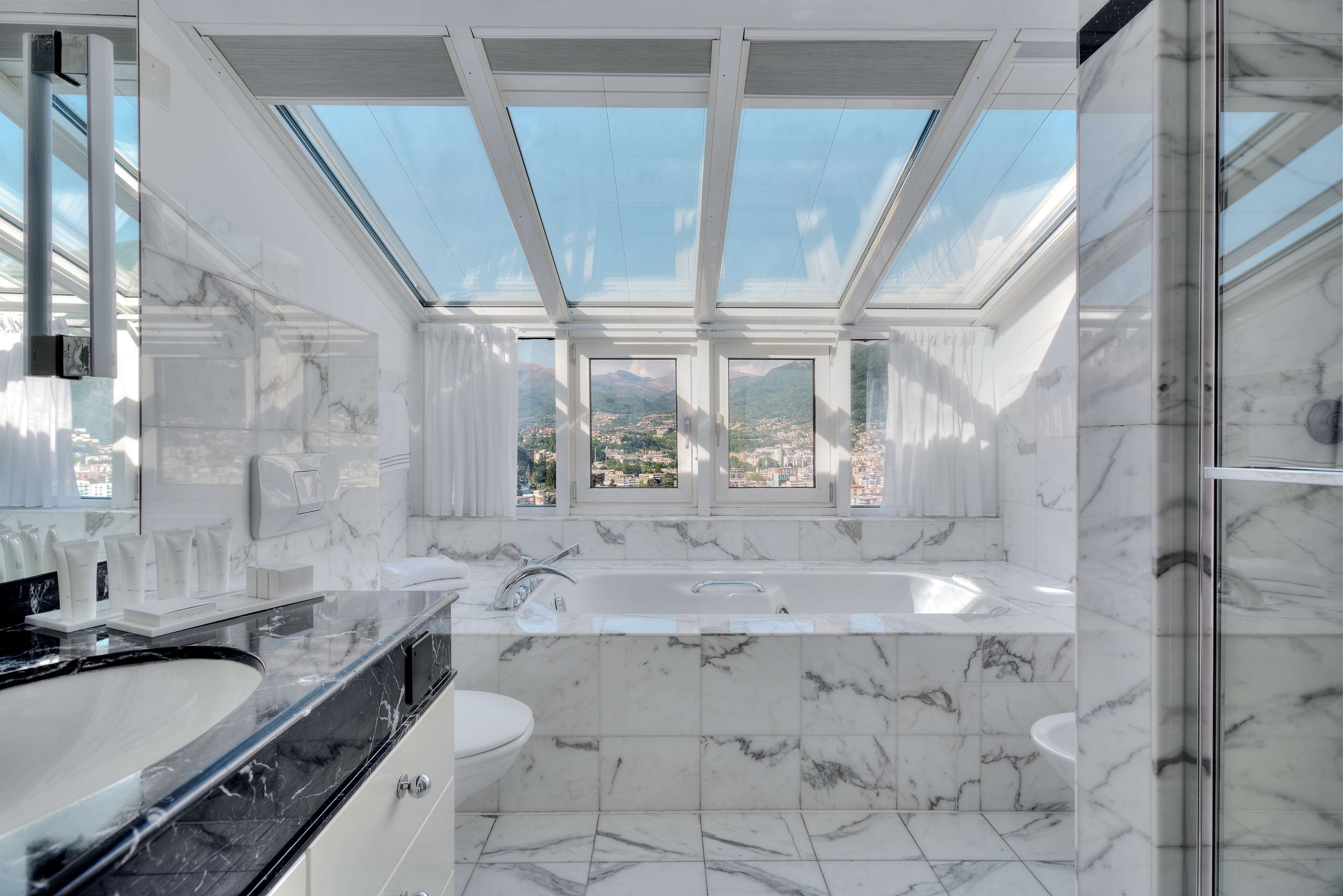 A modern bathroom with a skylight, a large bathtub, and a view of a cityscape.